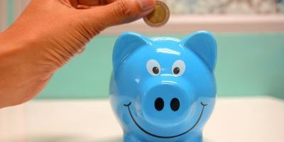 A person saving money by putting a coin into a piggy bank.